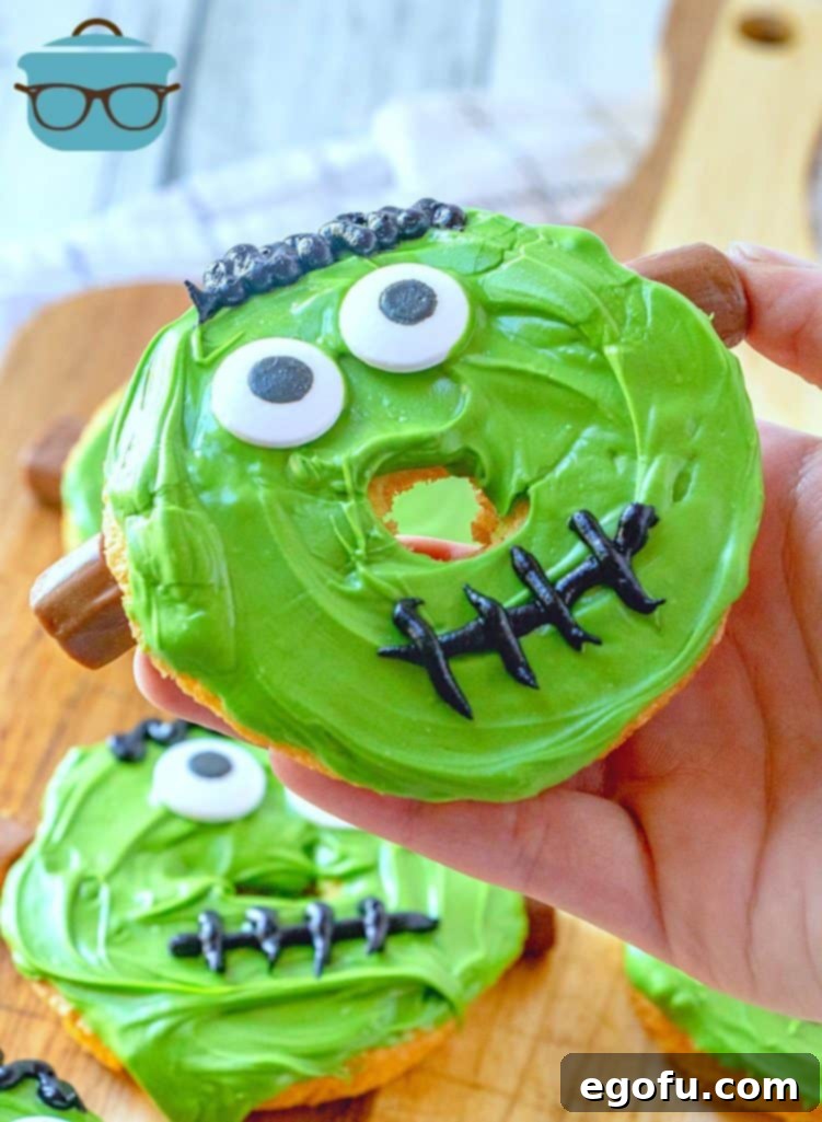 A tray of finished, decorated Frankenstein Doughnuts, complete with green faces, candy eyes, black icing hair and mouths, and Tootsie Roll bolts.