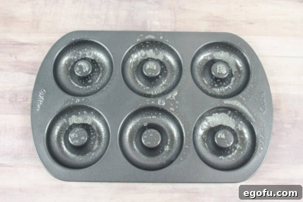 A 6-doughnut pan being sprayed with nonstick cooking spray, ready for batter.