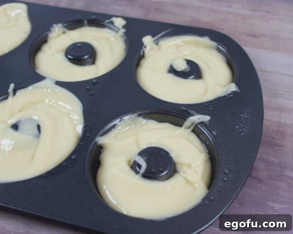 Cake mix batter carefully poured into a donut pan, filling each cavity evenly.
