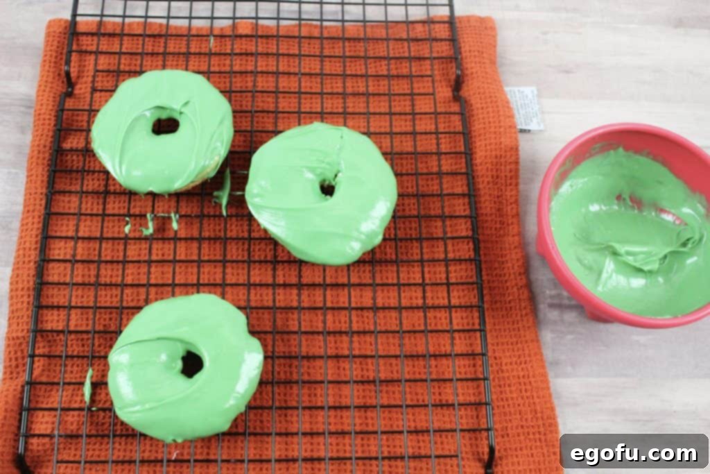 Several doughnuts, freshly dipped in green candy melts, set on a cooling rack.