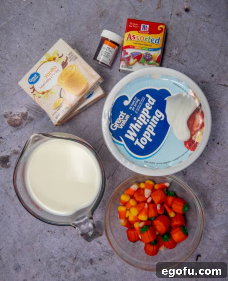 A colorful array of ingredients laid out for Candy Corn Pudding Parfaits, including boxes of instant vanilla pudding mix, a carton of cold milk, small bottles of yellow and orange food coloring, a tub of frozen whipped topping (COOL WHIP), and a festive scattering of candy corn and pumpkin candies.