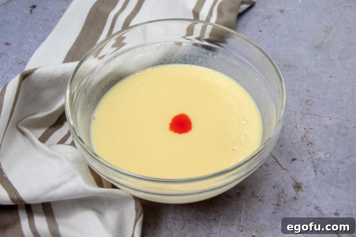 A clear glass mixing bowl holds a perfectly blended orange-colored vanilla pudding, created by mixing instant vanilla pudding, cold milk, and orange food coloring, ready for layering.