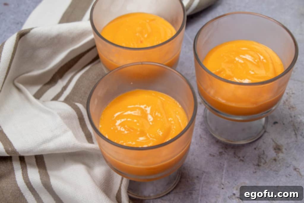 Rows of clear dessert glasses, each showcasing a neat bottom layer of orange-colored vanilla pudding, chilled and ready for the next layer.