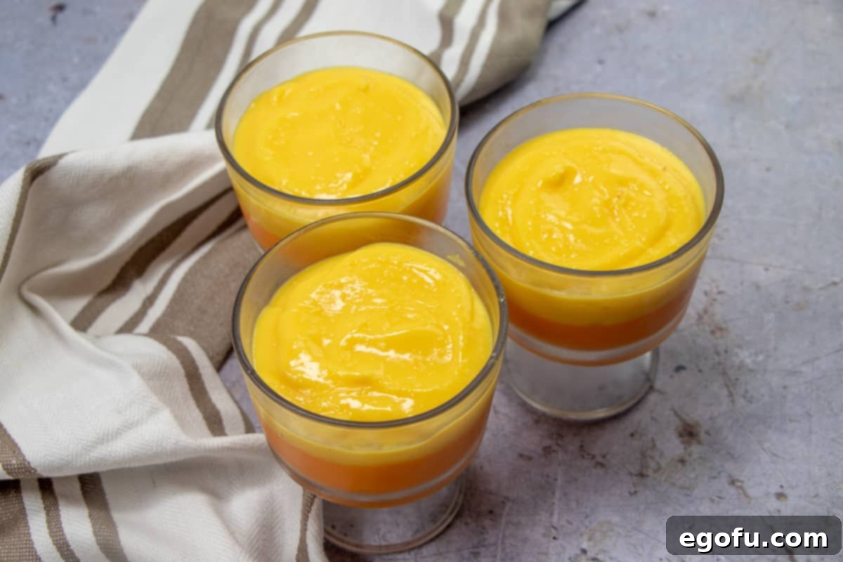 Clear glass dessert glasses with two distinct layers: a set orange vanilla pudding base, topped with a smooth, golden yellow vanilla pudding layer, chilling to perfection.