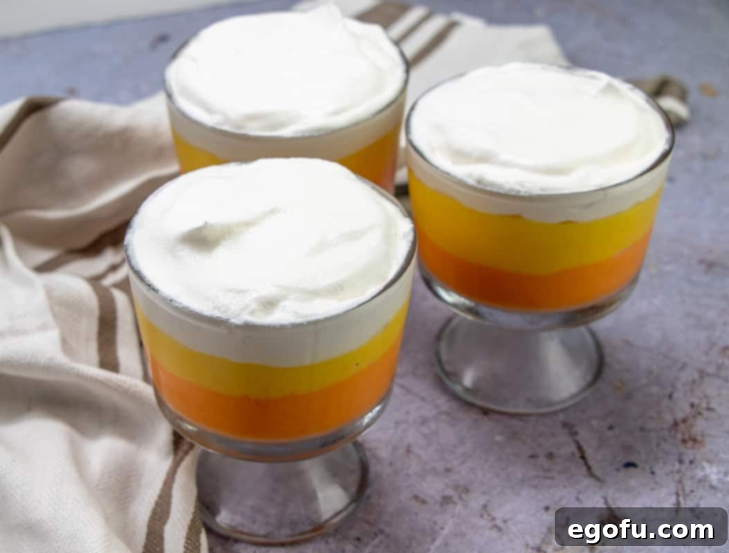 Rows of cooled pudding parfaits, each generously topped with a dollop of fluffy Cool Whip (whipped topping), completing the classic candy corn look.