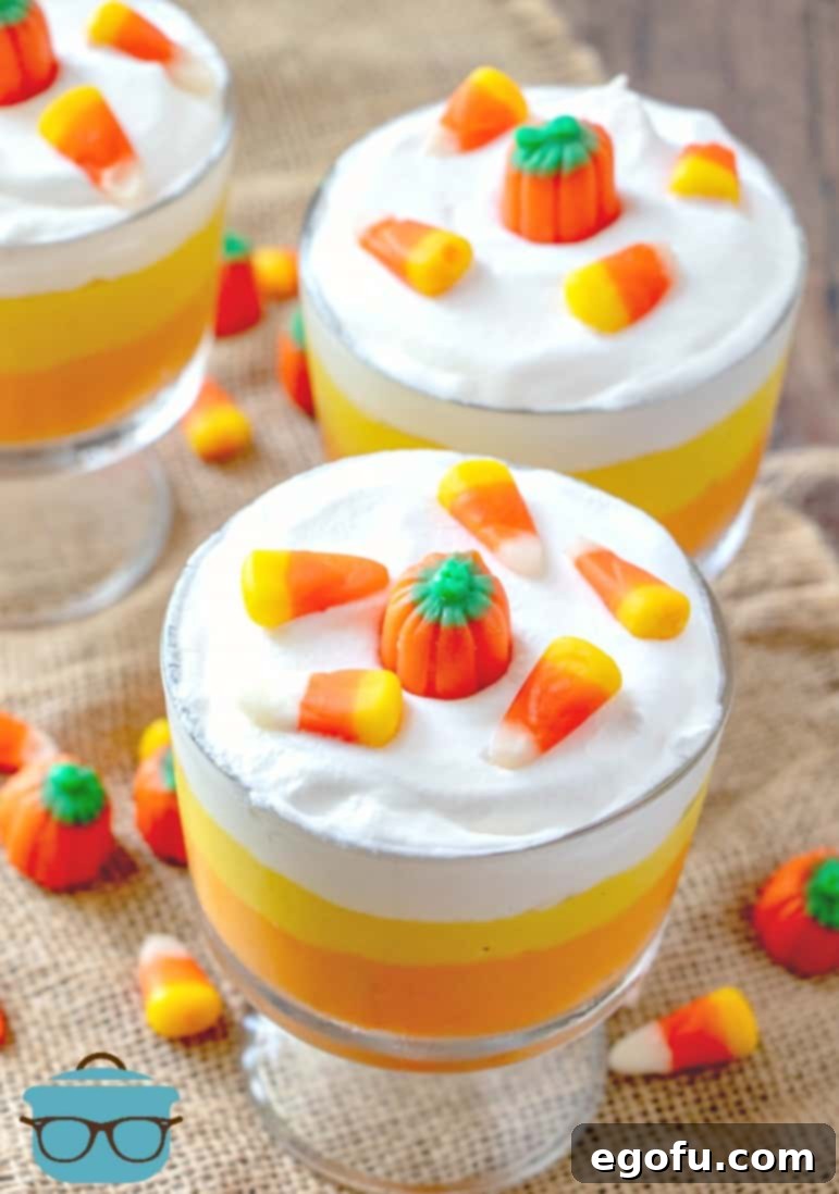 A dazzling close-up of a finished Candy Corn Pudding Parfait, beautifully topped with a swirl of whipped cream, an inviting candy corn piece, and a cheerful mallow creme pumpkin, perfectly capturing the spirit of Halloween.