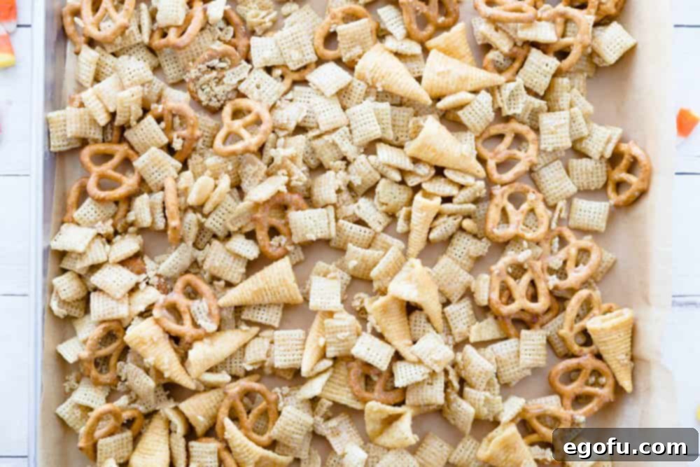Sweet fall, harvest chex mix shown on a baking sheet with natural colored parchment paper, spread out for even baking.