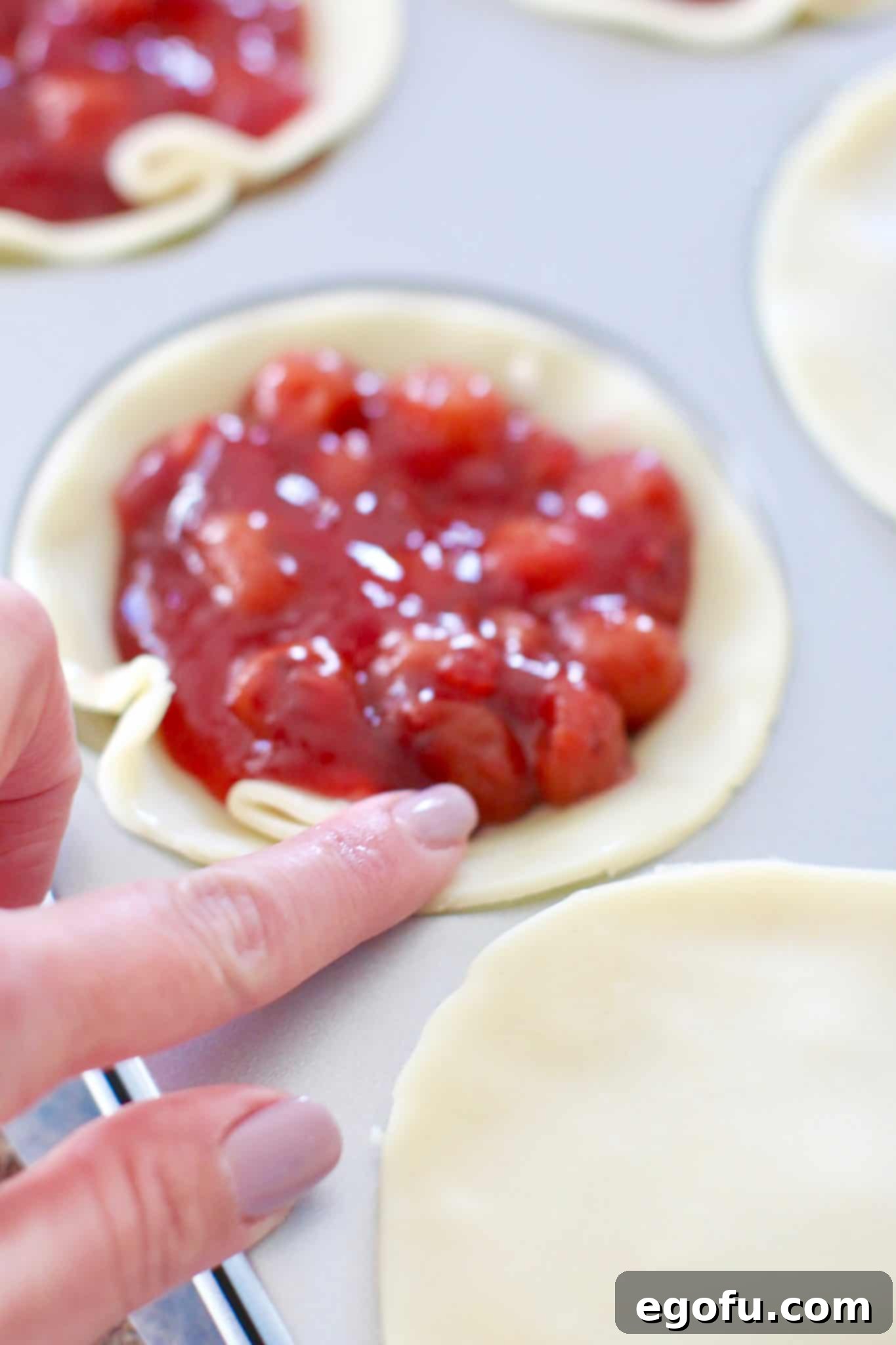Cherry Cheesecake Minis 12 A finger gently brushing egg wash along the inner rim of a pie crust, preparing it for the top layer.