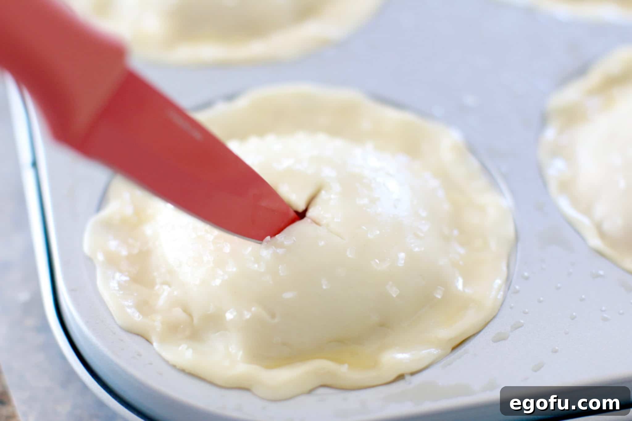 Cherry Cheesecake Minis 16 A small knife carefully cutting two slits into the top crust of a mini pie, creating vents for steam release during baking.