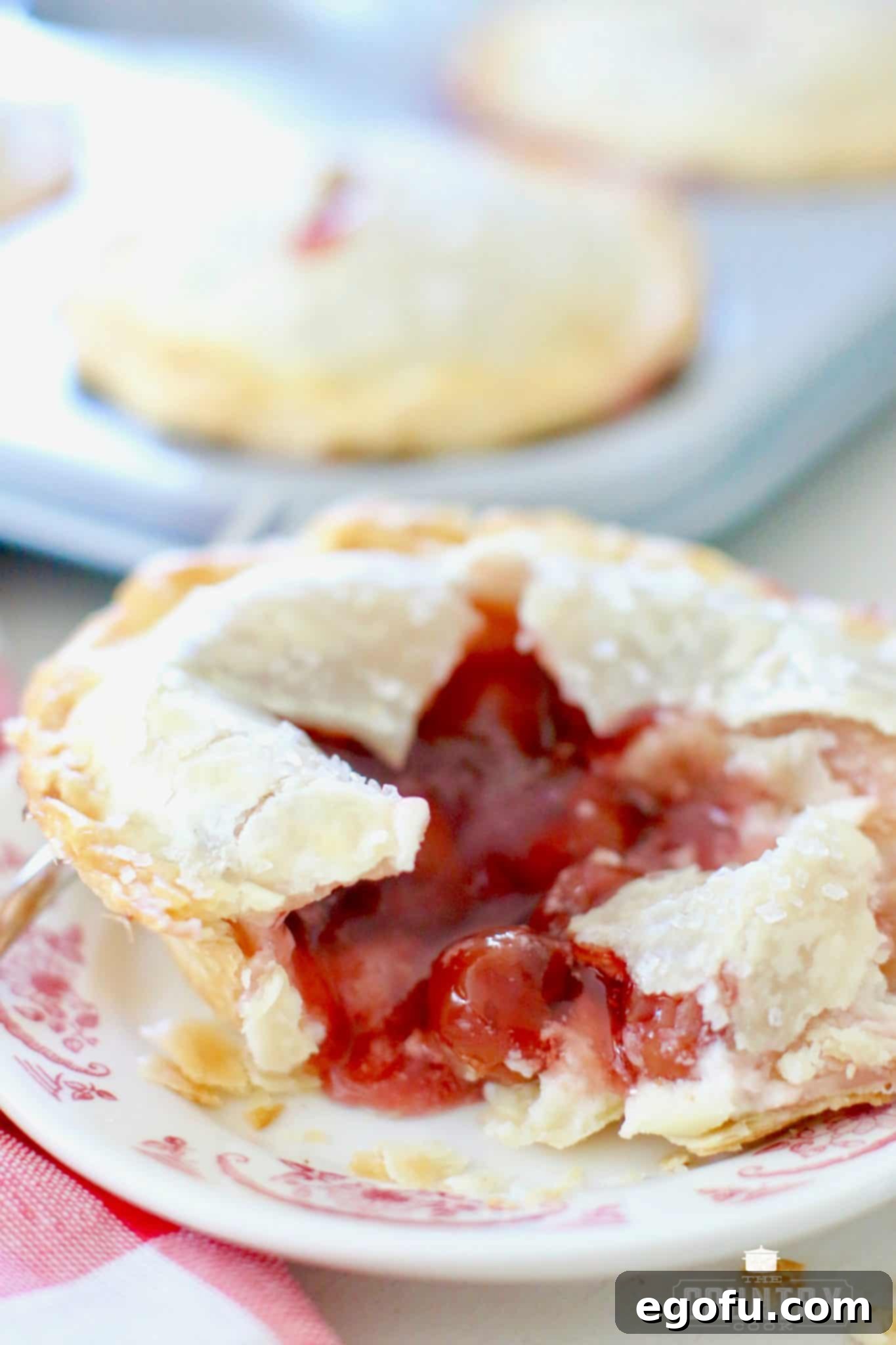 Cherry Cheesecake Minis 18 A single mini cherry cheesecake pie on a plate, cut open to reveal the luscious layers of cheesecake and cherry filling, inviting a taste.