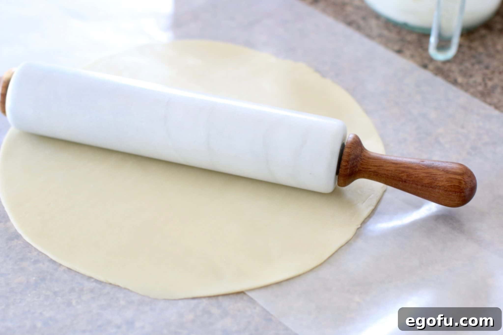 Cherry Cheesecake Minis 5 A Pampered Chef Marble Rolling Pin being used to gently flatten a refrigerated pie crust on wax paper, preparing it for cutting.
