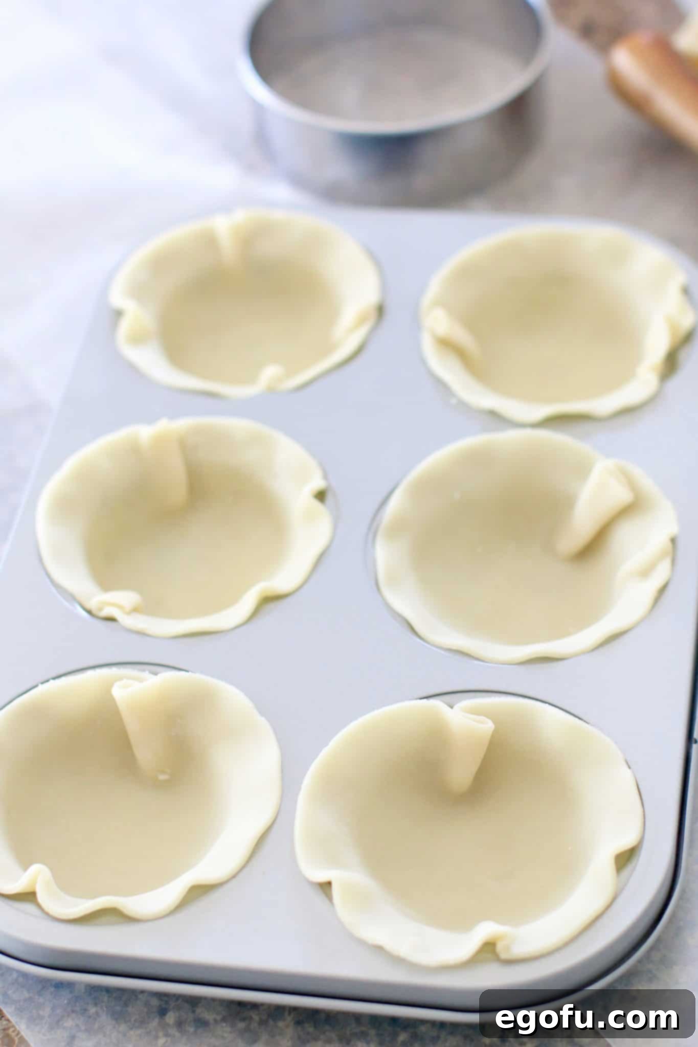 Cherry Cheesecake Minis 7 Pie crust dough circles carefully pressed into the individual wells of a mini pie pan, forming the foundation of the pies.