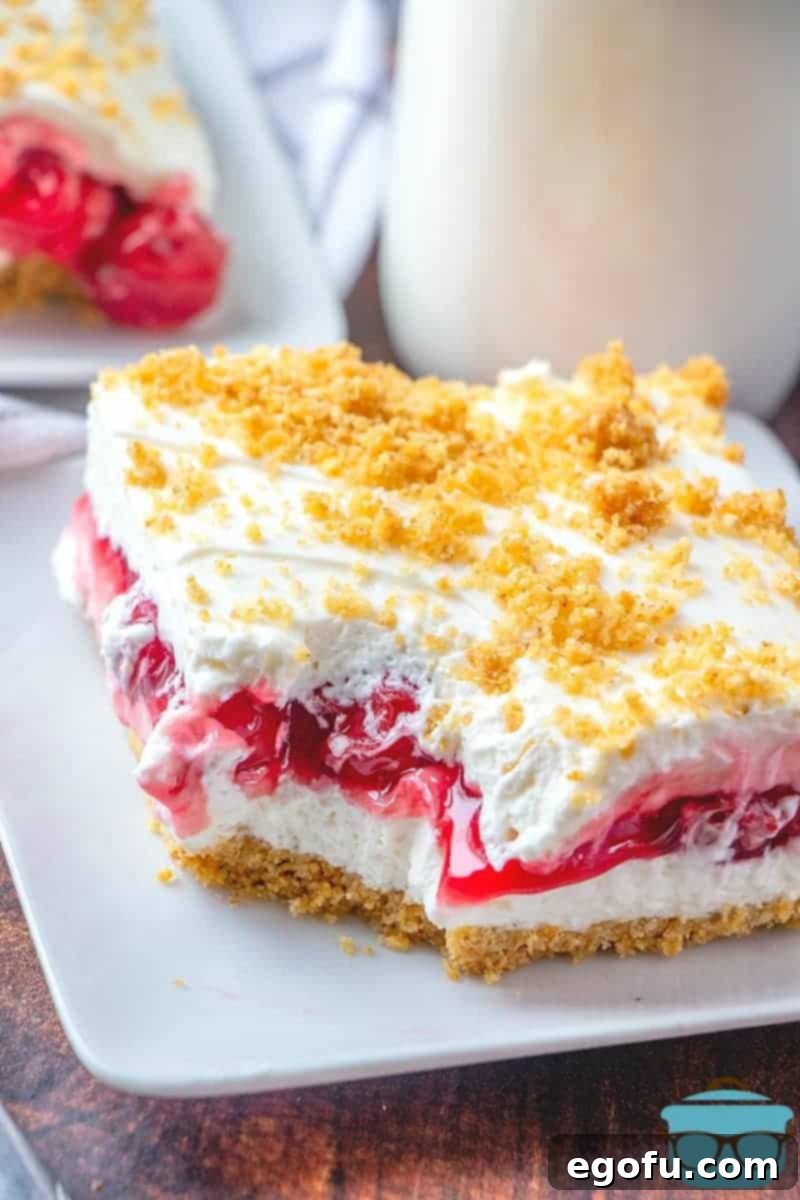 A delectable slice of No-Bake Cherry Yum Yum layered dessert resting on a white plate, with a glass of milk in the soft-focus background, highlighting its vibrant layers.
