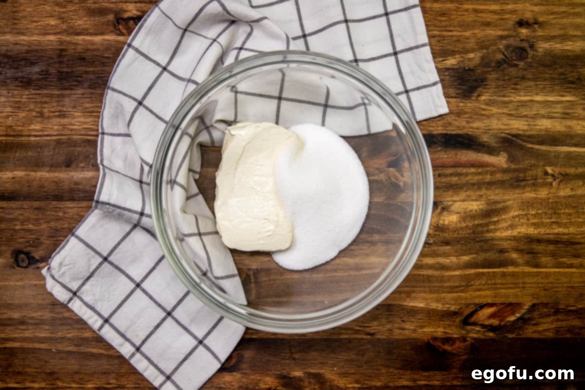 Softened block of cream cheese and granulated sugar at the bottom of a medium glass bowl, ready to be beaten for the creamy layer.