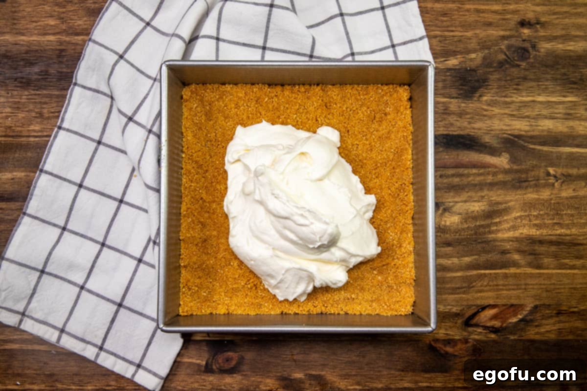 Half of the cream cheese and whipped cream mixture smoothly spread over the graham cracker crust in the baking pan, forming an even white layer.