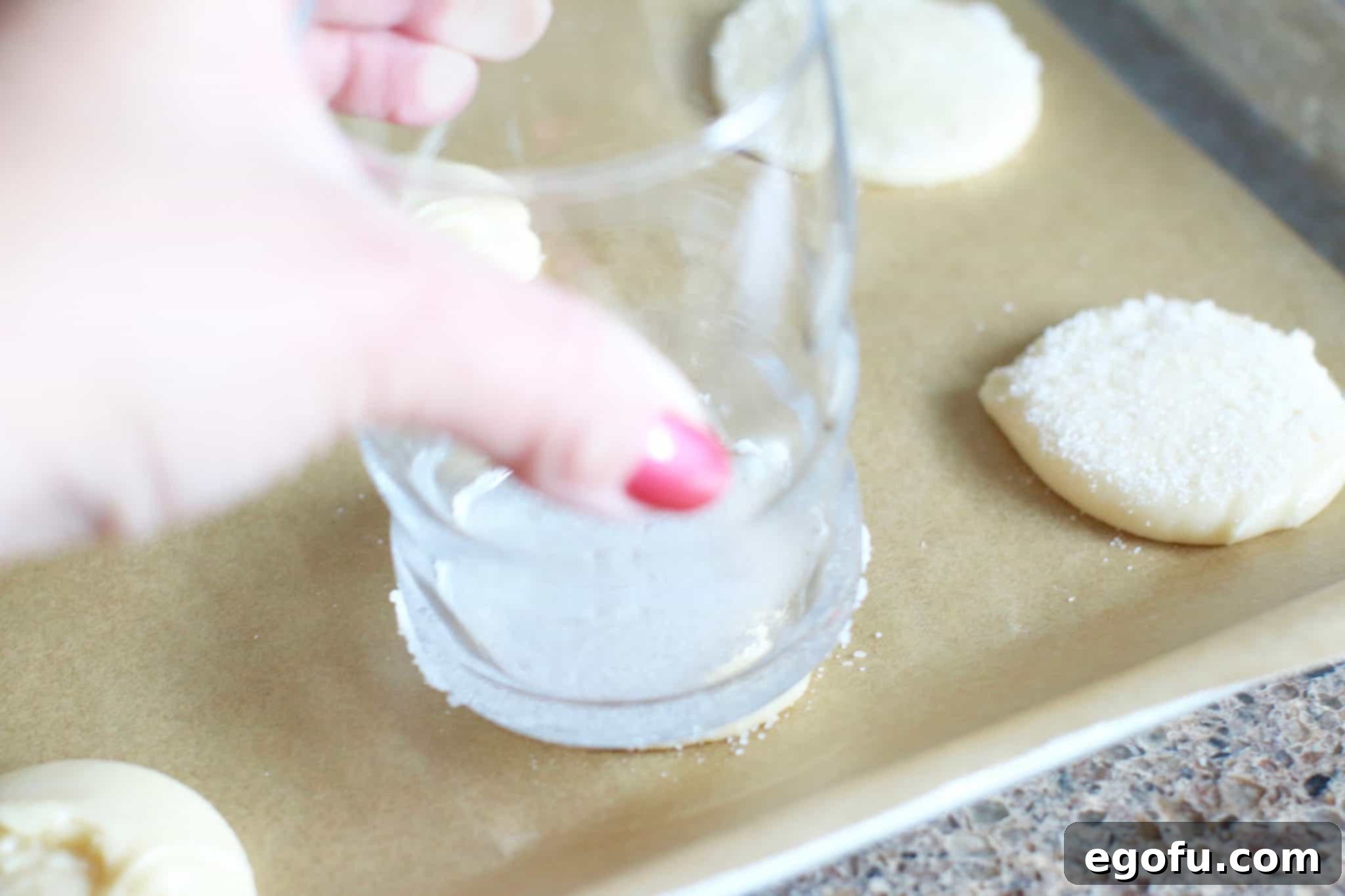Sugar-coated glass gently pressing down onto cookie dough mounds.