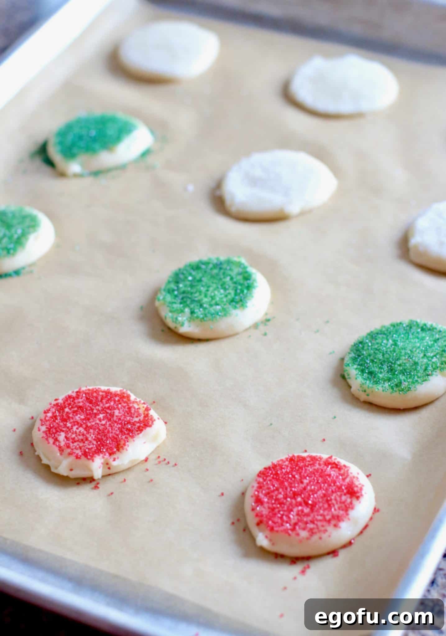 Baking sheet with unbaked Christmas sugar cookies, each gently pressed with colored sugar.
