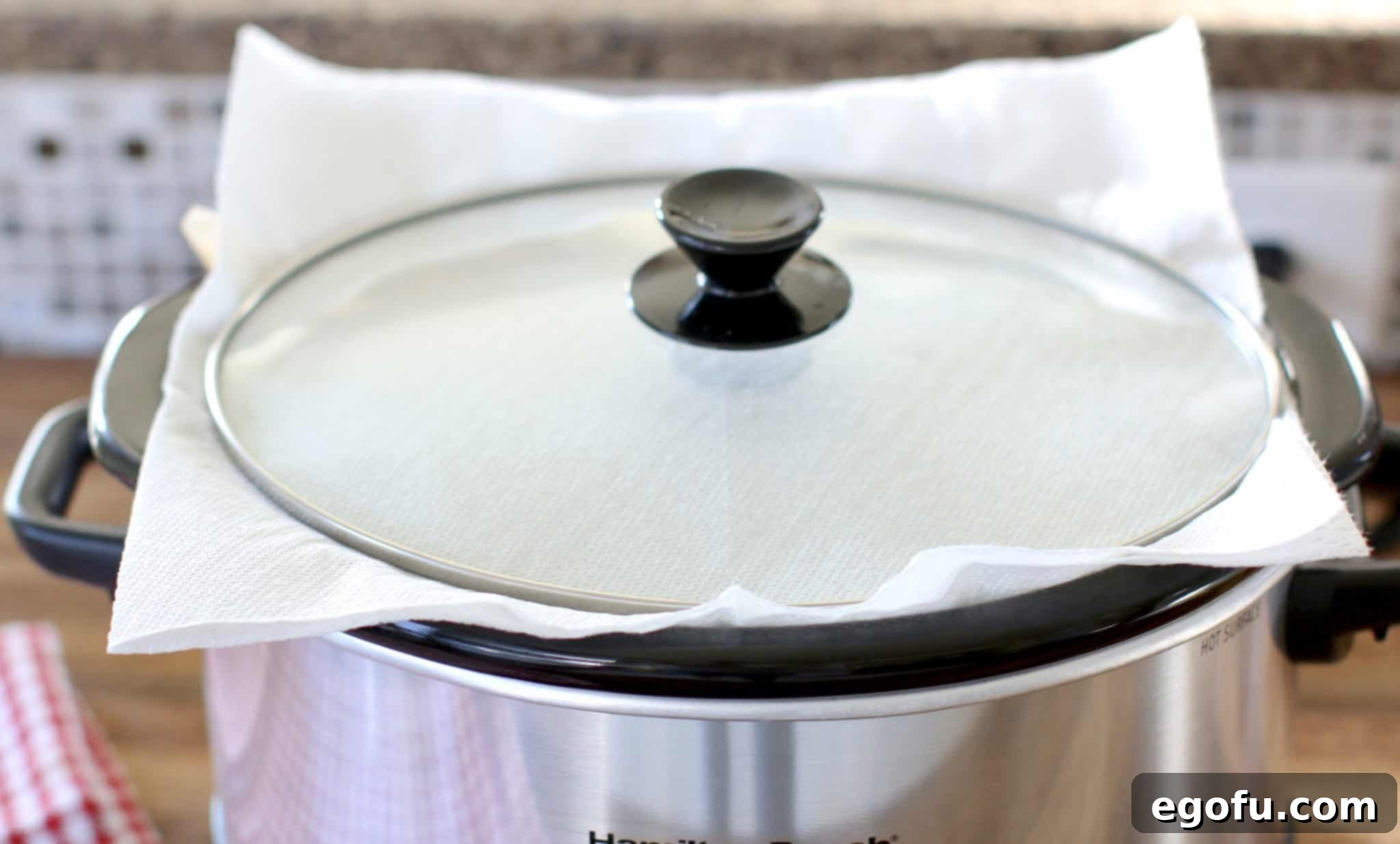 A close-up shot of paper towels carefully placed under the lid of a slow cooker, illustrating the condensation absorption technique.