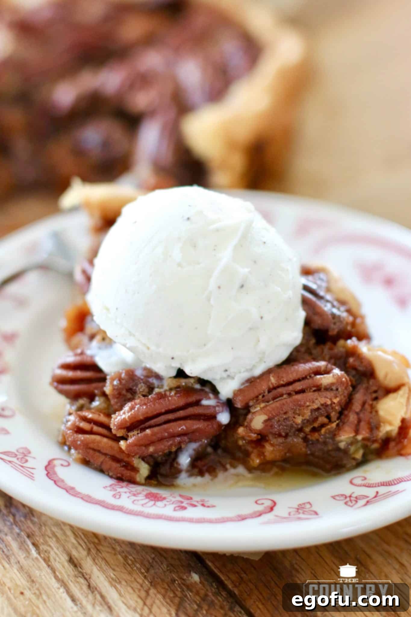 A perfect slice of Slow Cooker Pecan Pie on a white plate, topped with a scoop of melting vanilla ice cream, ready to be enjoyed.