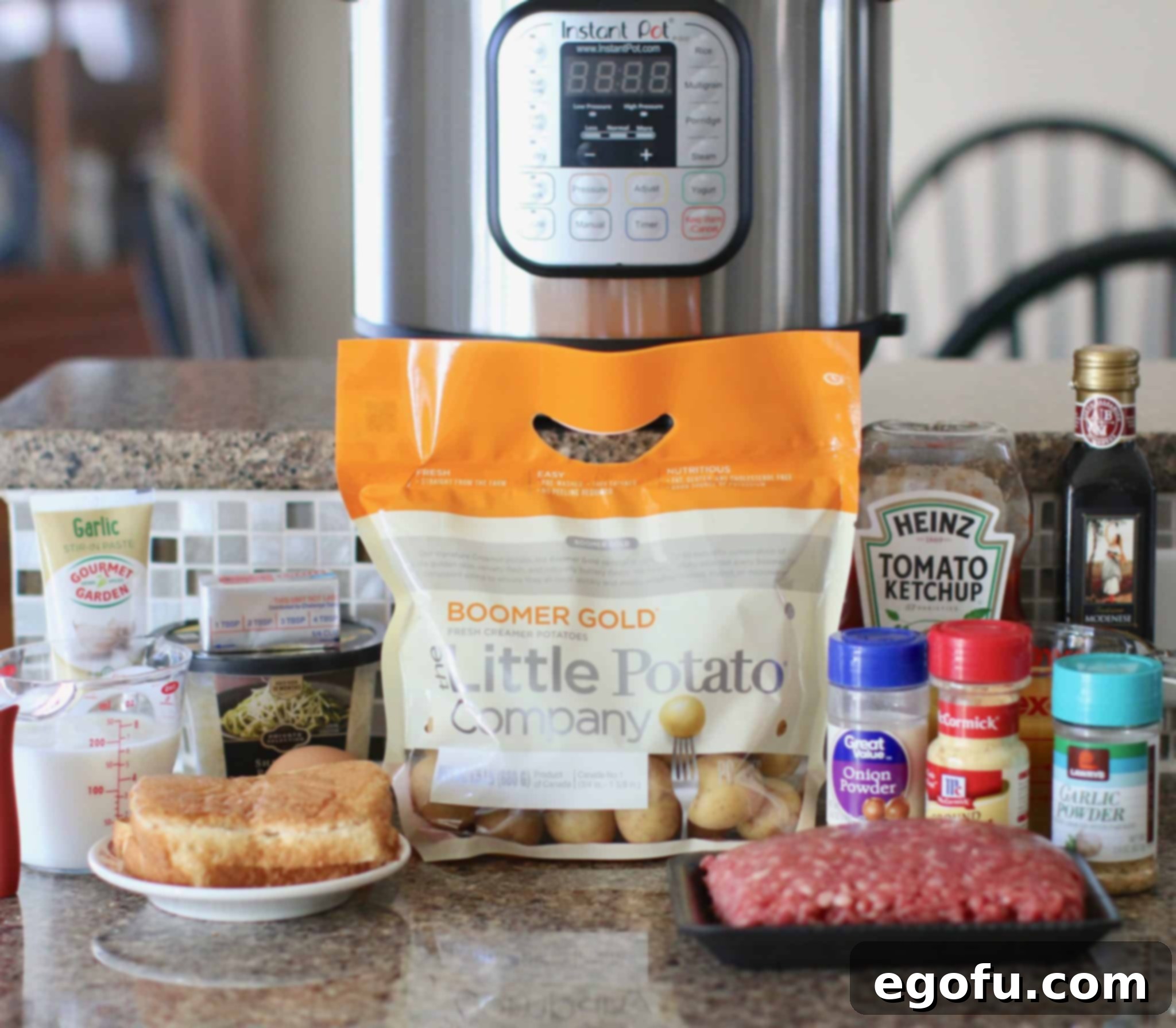 An array of fresh ingredients laid out for Instant Pot Meatloaf and Garlic Parmesan Potatoes, including potatoes, garlic, parmesan, lean ground beef, egg, ketchup, balsamic vinegar, onion powder, garlic powder, and ground mustard.