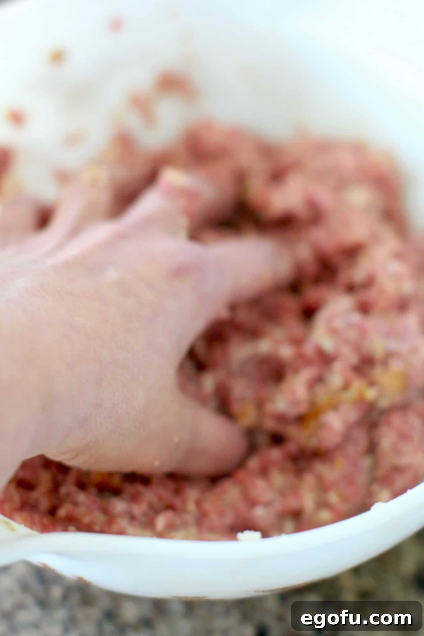 A hand gently mixing the meatloaf mixture in a bowl, ensuring all ingredients are evenly distributed.