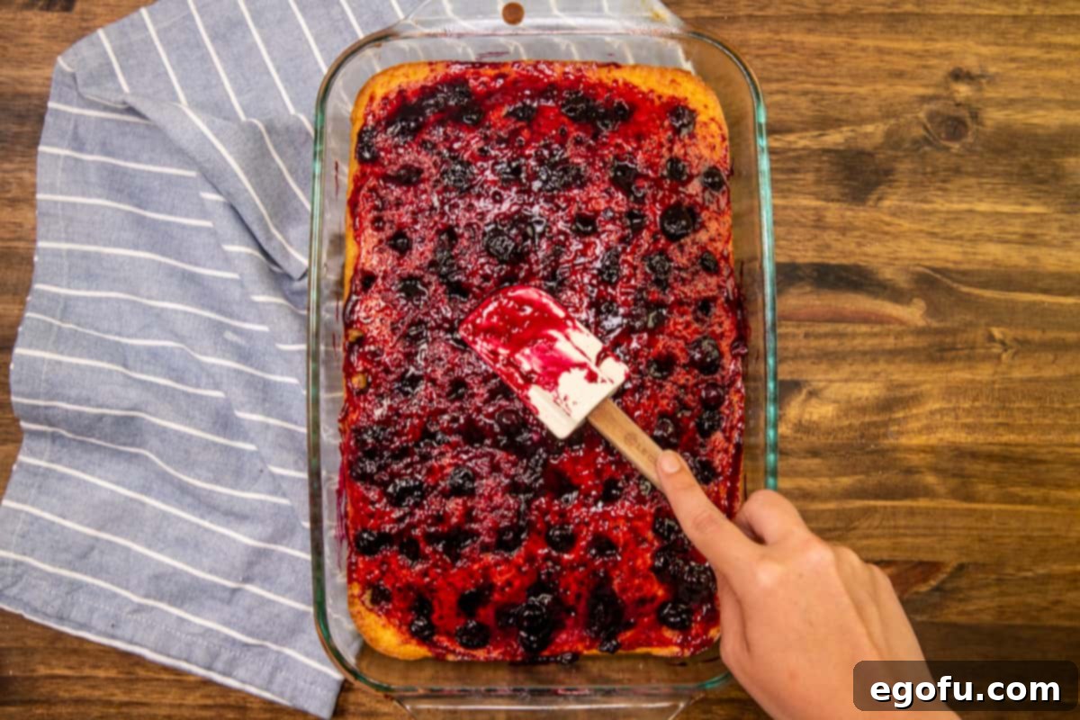 spreading lemon blueberry sauce onto baked lemon cake with a spreader.