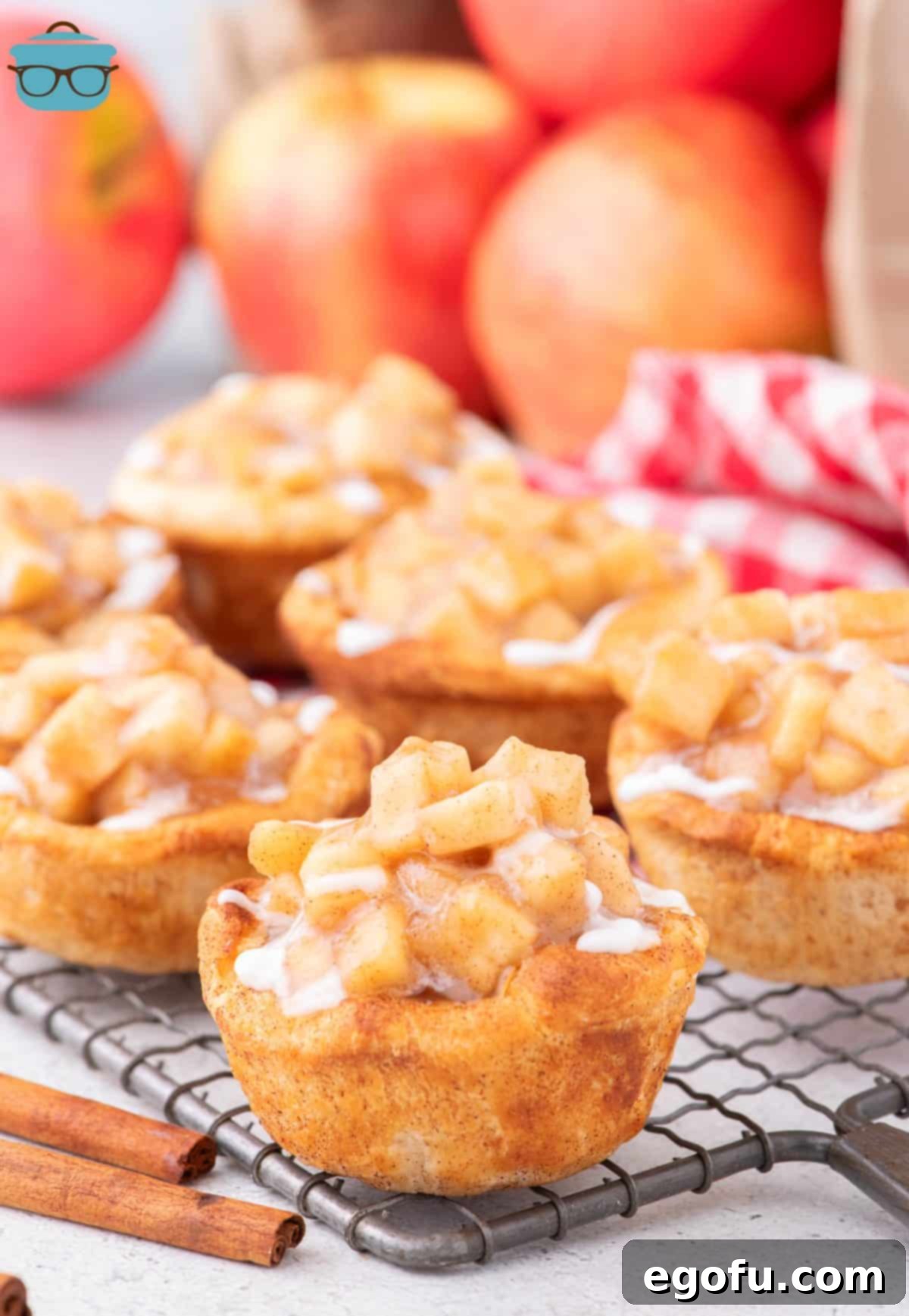 A close-up view of freshly baked Apple Pie Cinnamon Rolls cooling on a wire rack, glistening with sweet glaze.