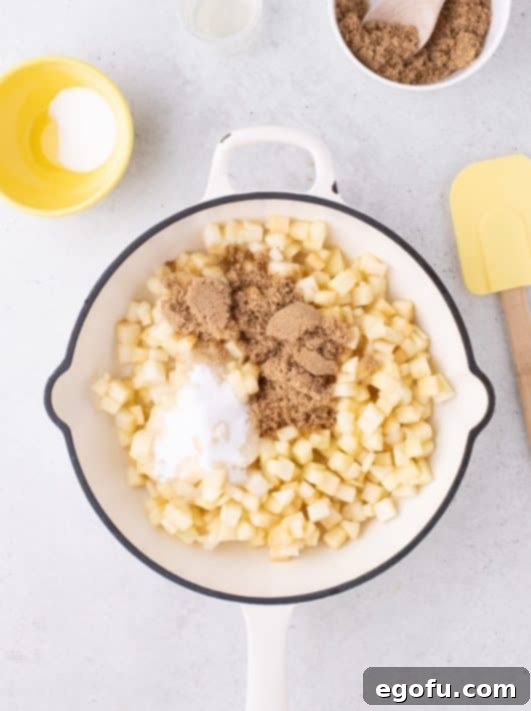 Diced apples with granulated sugar, brown sugar, and lemon juice cooking in a skillet.