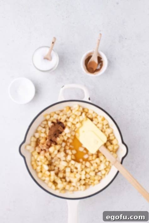 Cinnamon, nutmeg, and salt being added to the simmering apple mixture in a skillet.