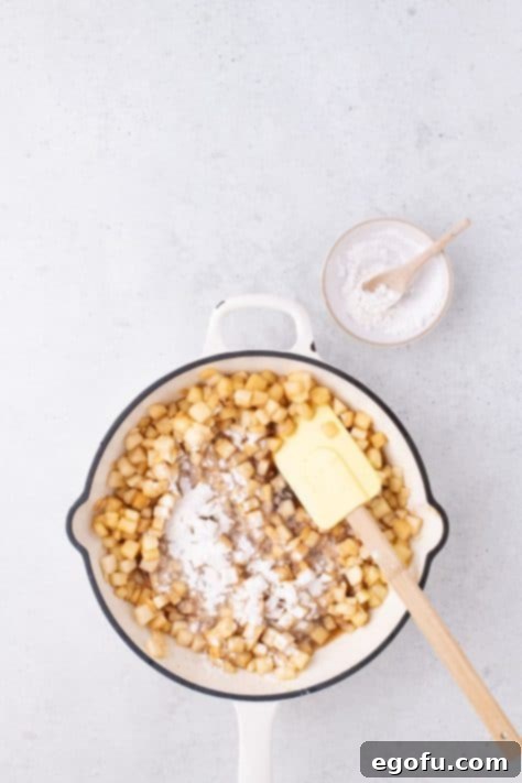 Flour being stirred into the apple pie filling as it thickens in the skillet.