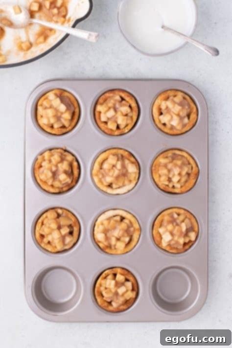 Apple pie filling carefully spooned into individual biscuit cups in a muffin tin.