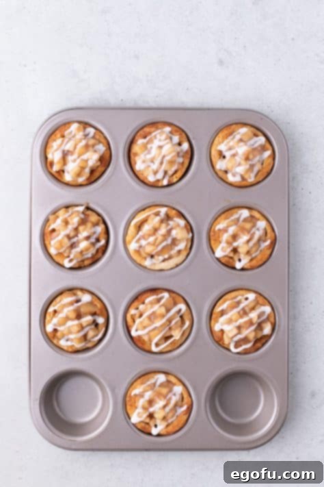 Sweet glaze being drizzled over freshly filled Apple Pie Cinnamon Rolls in a muffin pan.