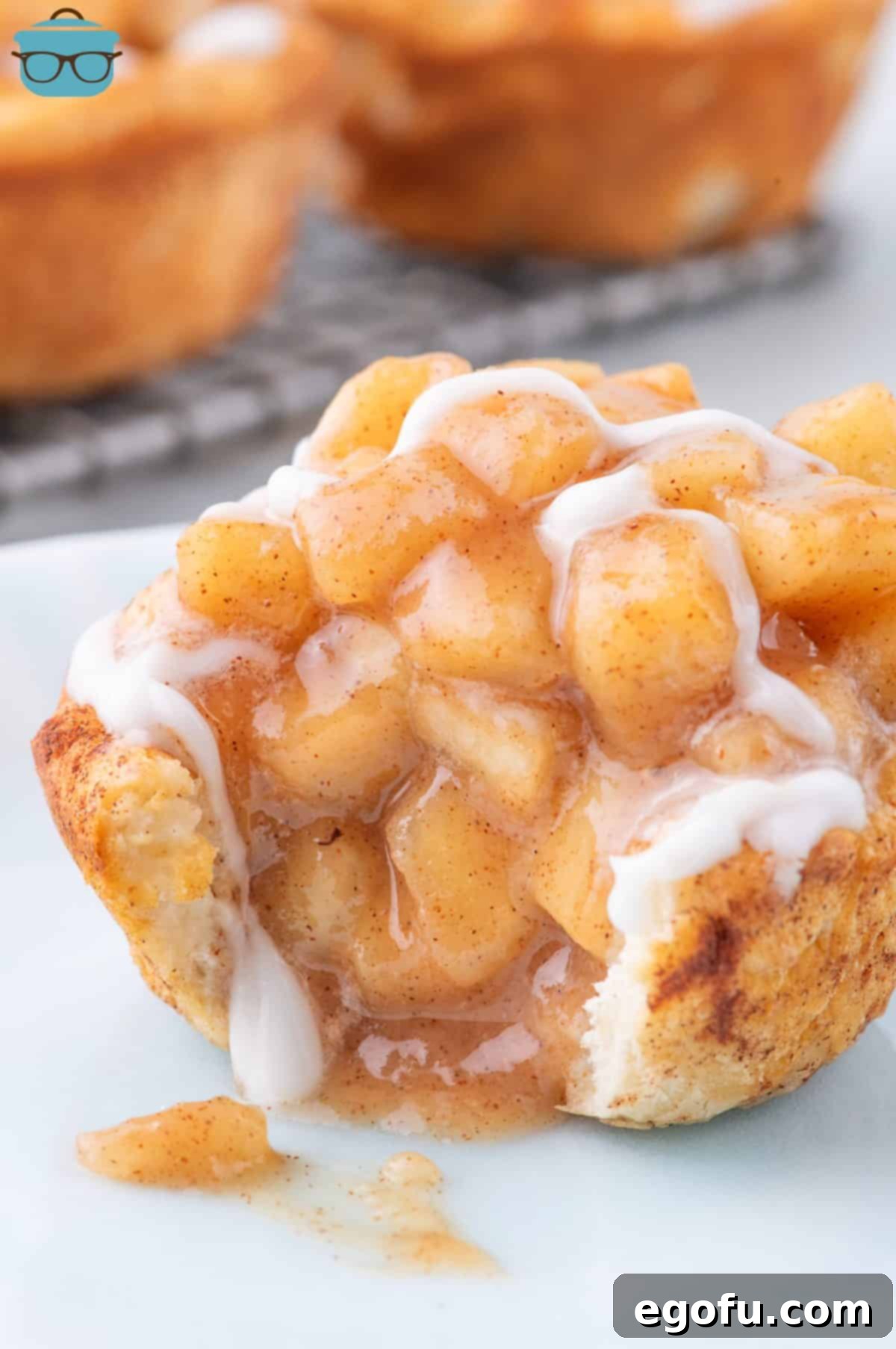 A single Apple Pie Cinnamon Roll with a bite taken out, showcasing the vibrant apple filling and sweet glaze.