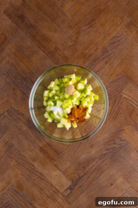 Diced apples, cinnamon, sugar, brown sugar, and vanilla extract mixed in a small clear bowl.