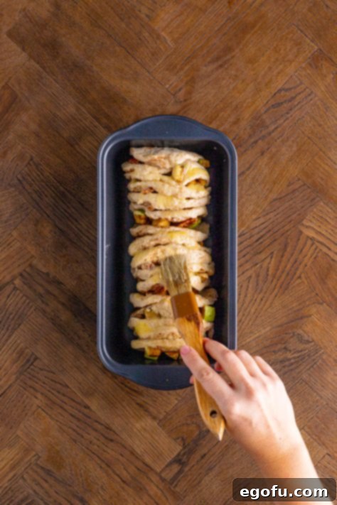 Brushing the top of biscuit stacks in the loaf pan with melted butter.