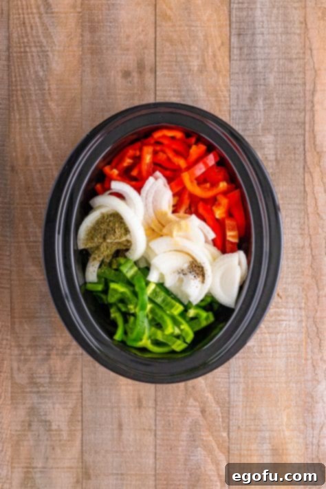 Sliced onions, peppers and seasonings in a crock pot.