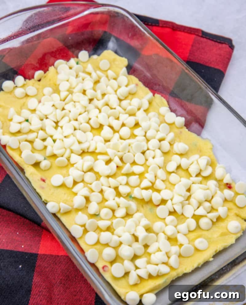 White chocolate chips sprinkled over the first layer of cake mix batter in a baking pan.