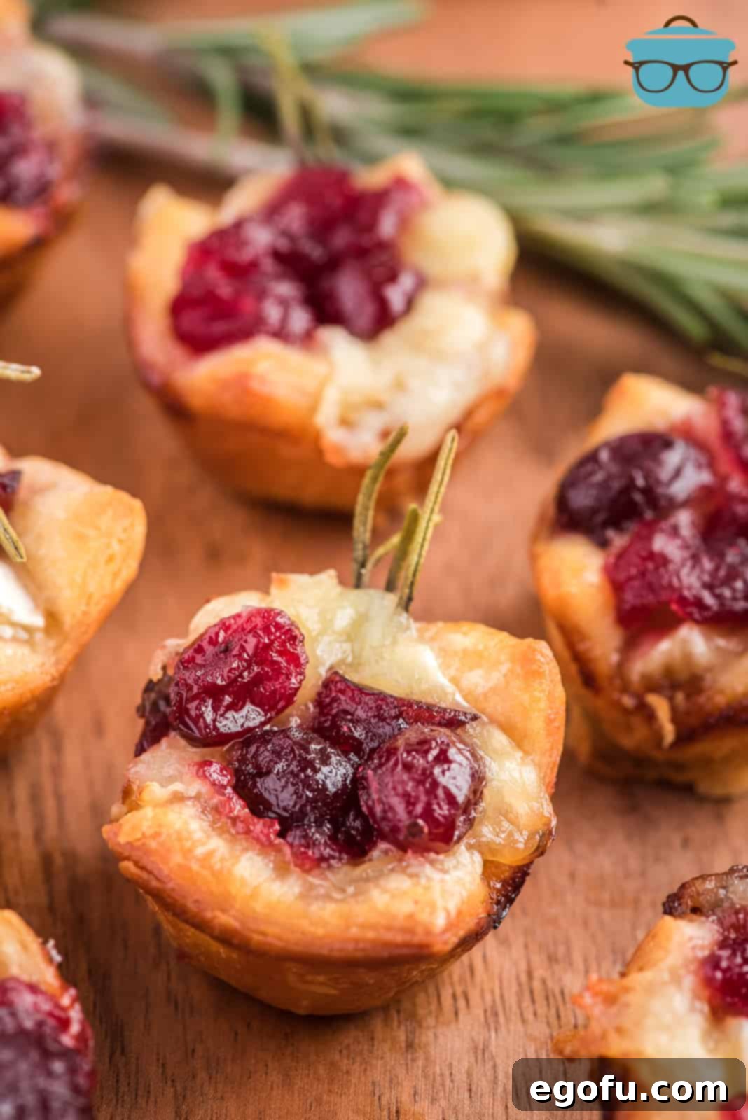 Golden Cranberry Brie Delights 2 Close-up photo of a cooked Cranberry Brie Bite on a wooden surface, garnished with rosemary.