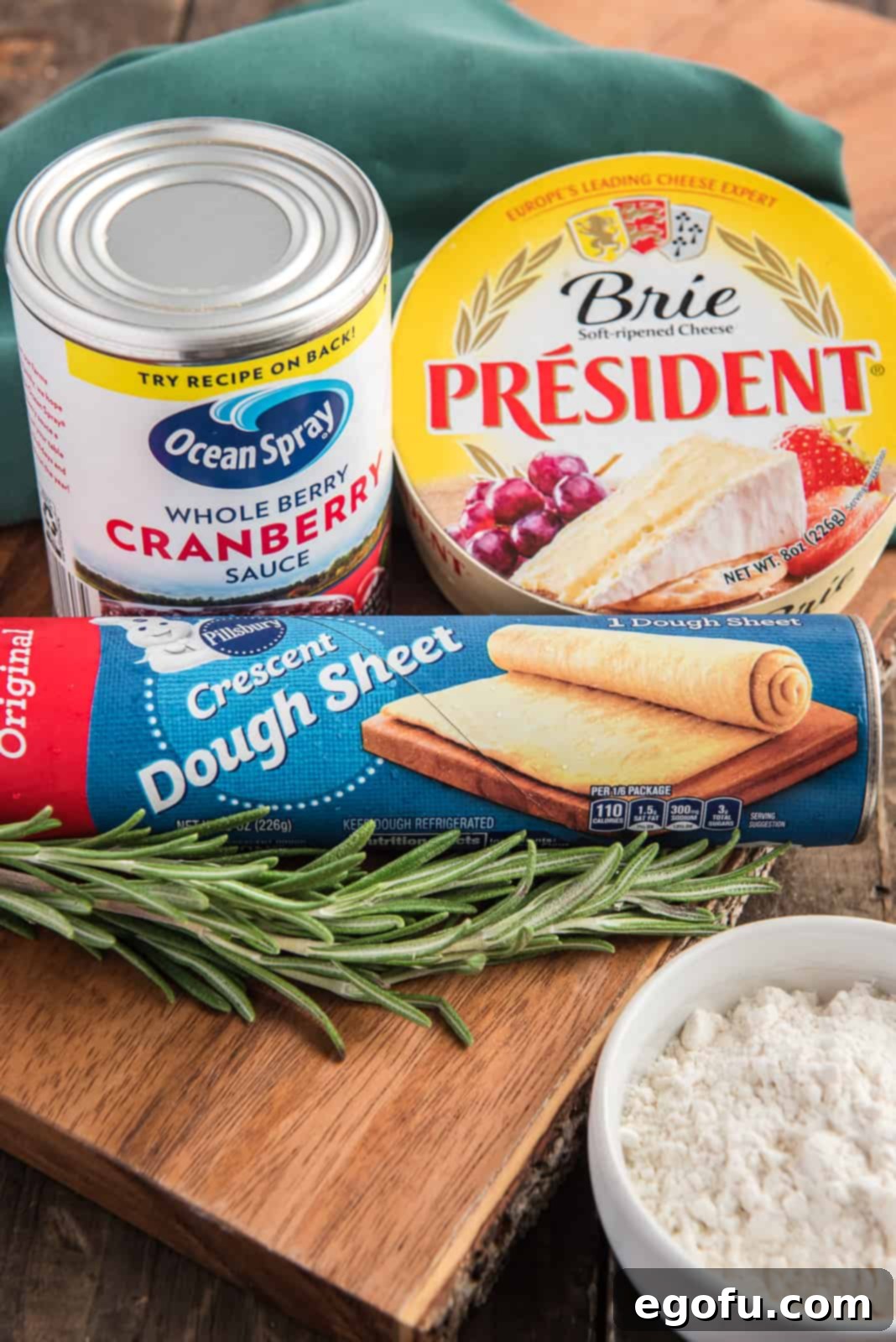 Golden Cranberry Brie Delights 4 Ingredients for Cranberry Brie Bites: flour, brie cheese, whole cranberry sauce, crescent roll dough, and fresh rosemary sprigs.
