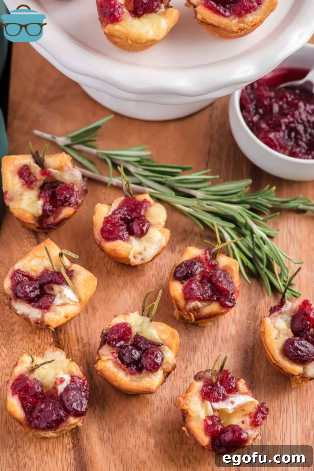 Golden Cranberry Brie Delights 8 Several cranberry brie bites arranged on a rustic wooden surface with a white cake pedestal in the background, ready for serving.