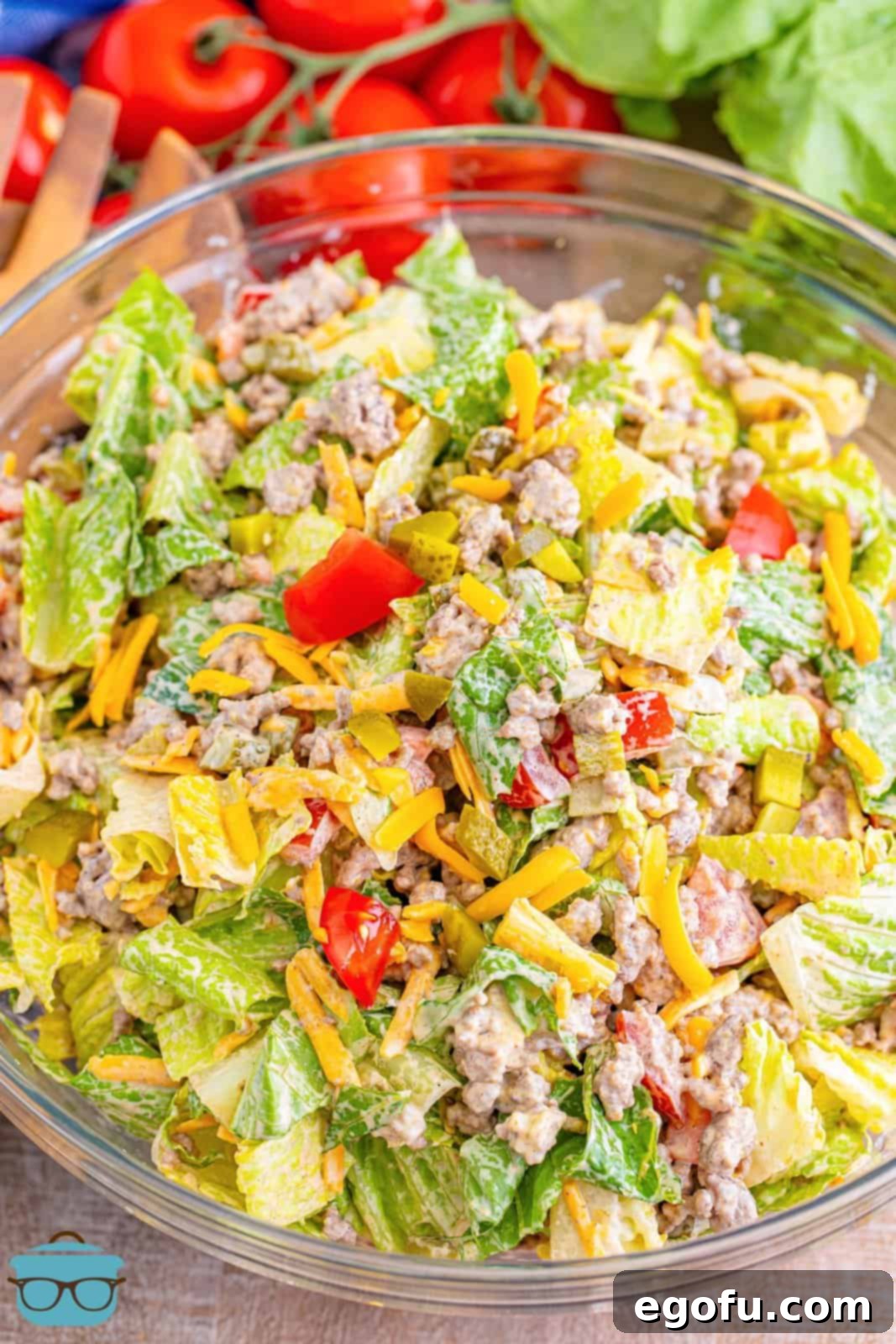 A large glass bowl filled with a vibrant Big Mac Salad, showcasing mixed lettuce, seasoned ground beef, shredded cheese, and a creamy dressing. Fresh ingredients are clearly visible, promising a delicious meal.