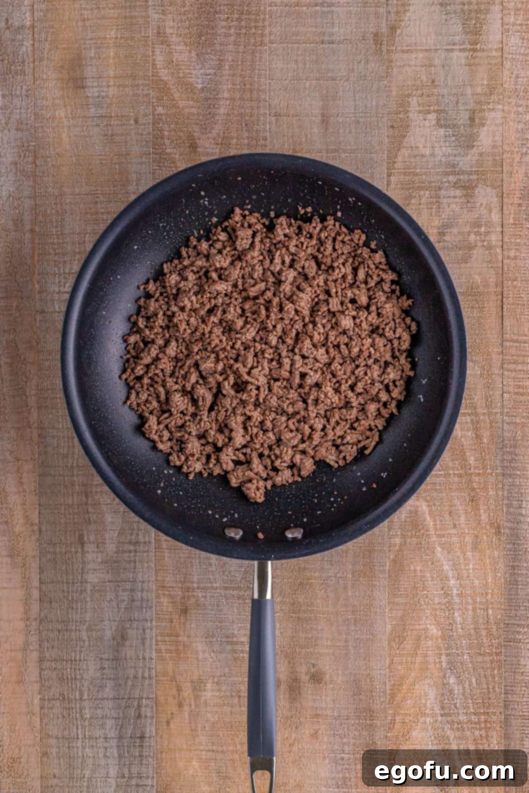 Cooked and crumbled ground beef shown in a large non-stick skillet, having been browned to perfection. The beef is ready to be drained of excess grease and added to the salad.