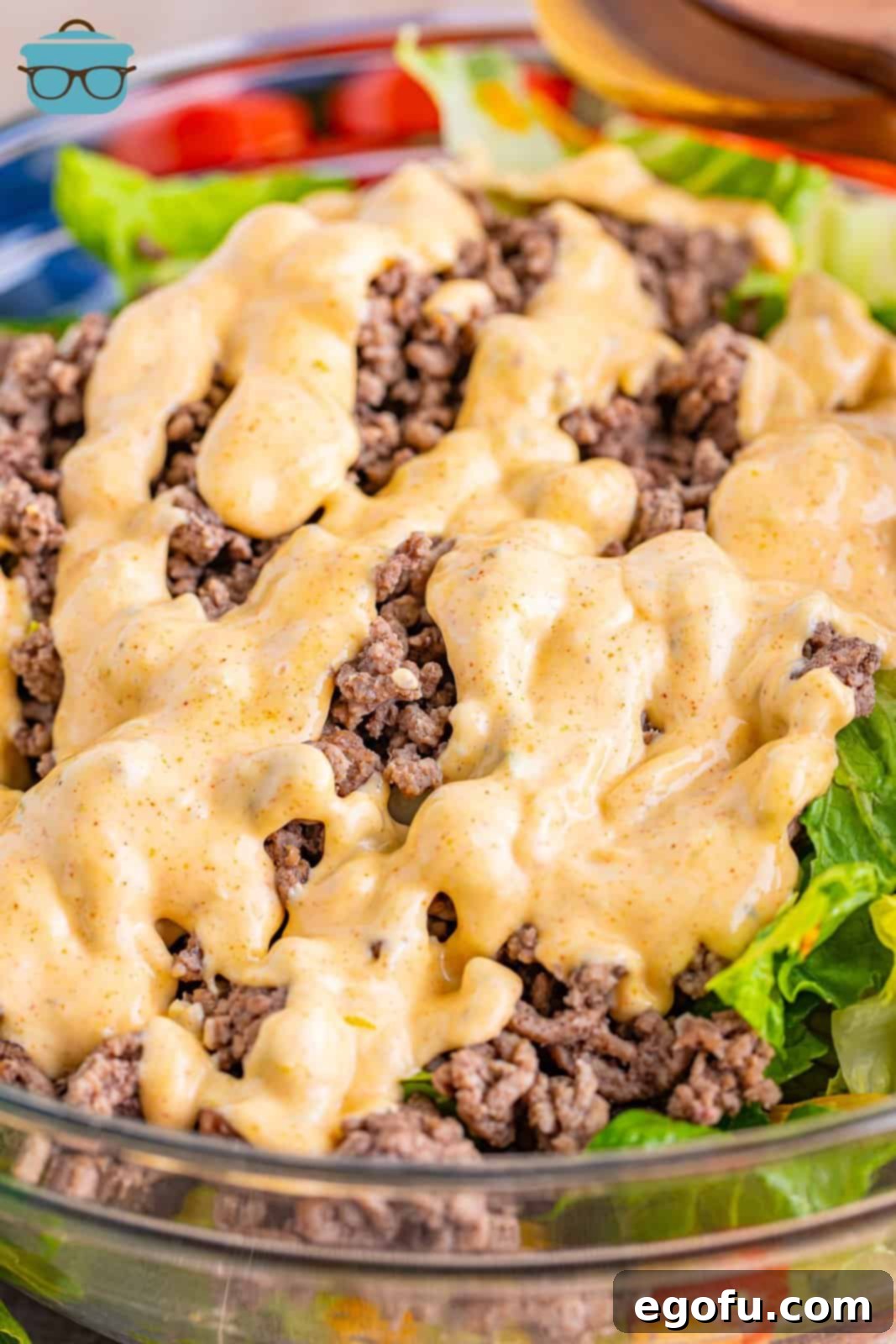 A close-up shot of the creamy Big Mac salad dressing being drizzled over the mixed salad ingredients in a clear bowl, highlighting the rich texture and inviting consistency of the sauce.