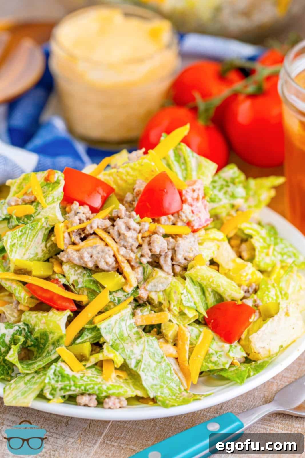 A perfectly portioned serving of mixed Big Mac Salad on a round white plate, with fresh tomatoes on the vine softly blurred in the background, suggesting a delightful and wholesome meal experience.