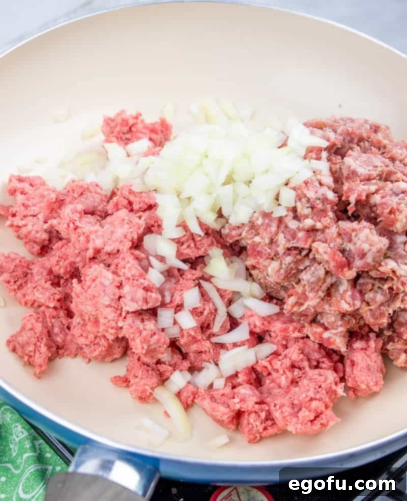 Ground beef, Italian sausage, and diced onion browning in a large skillet, seasoned with salt and pepper.
