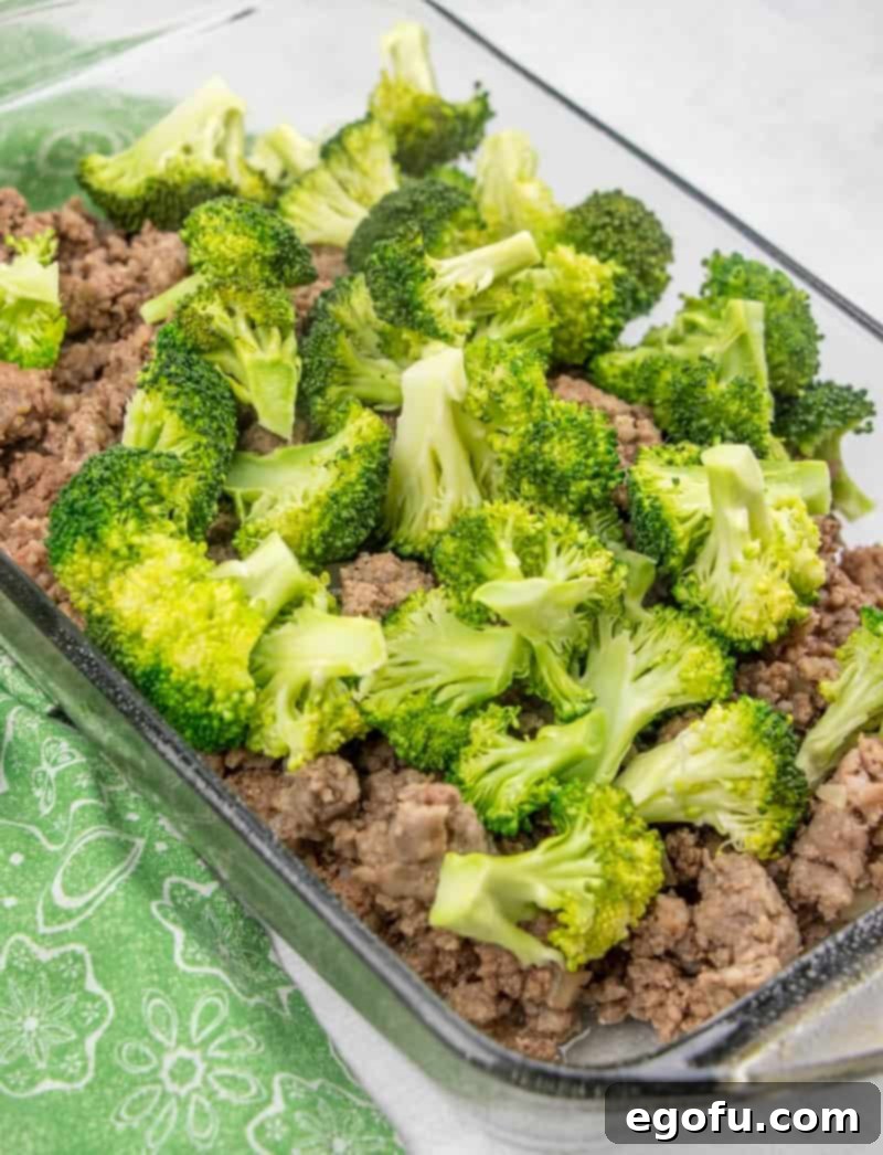 Cooked ground beef, Italian sausage, steamed broccoli, and creamy cheese sauce combined in a 9x13 baking dish, ready for the final touches.