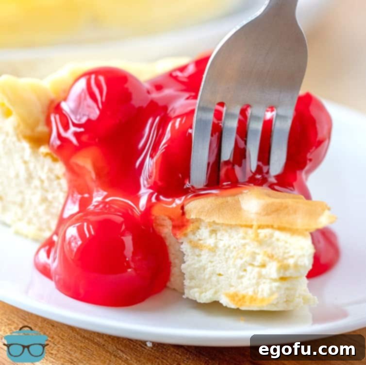 A fork scooping a bite of creamy low carb cherry cheesecake from a small white plate.