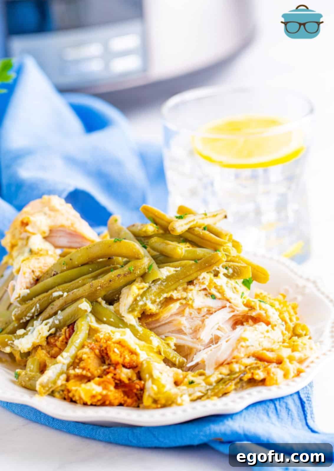 chicken, stuffing and green beans shown served on a round white plate with a glass of ice water in the background.