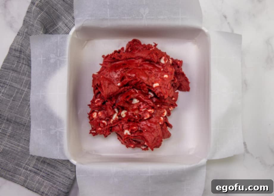 Velvet Red Dream Bars 6 thick red velvet batter with white chocolate chips in the bottom of a parchment paper-lined white, square baking dish.