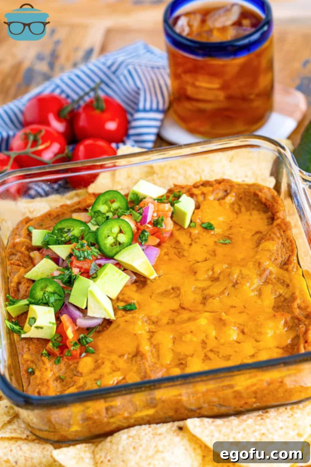 fully baked refried bean dip in a clear baking dish surrounded by tortilla chips and fresh tomatoes. 
